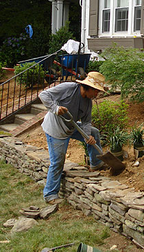 Rock wall with plantings and forest in the background.